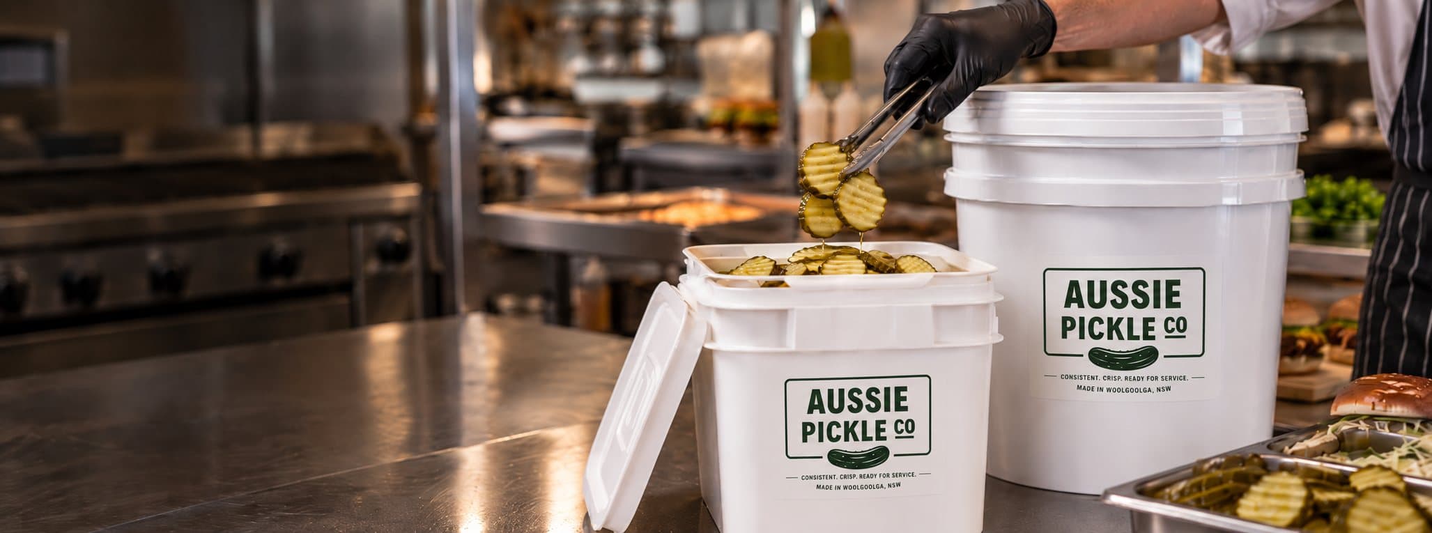 Chef lifting crinkle cut pickles from an Aussie Pickle Co 5L bucket, with a 20L bucket behind
